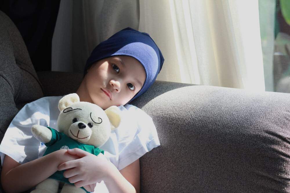 A child is holding a plush toy and getting prepared for chemotherapy